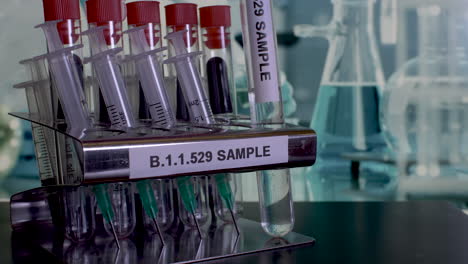 close up shot of medical glass test tubes being removed from a stainless steel rack labelled with b.1.1.529 sample, the scientific name for the new strain of corona virus omicron