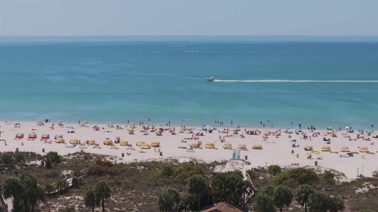 Aerial view of Gulf of Mexico from Saint Pete Beach showing white sand, turquoise waters, beachgoers with colorful umbrellas, and parasailing in Florida's premier beach destination