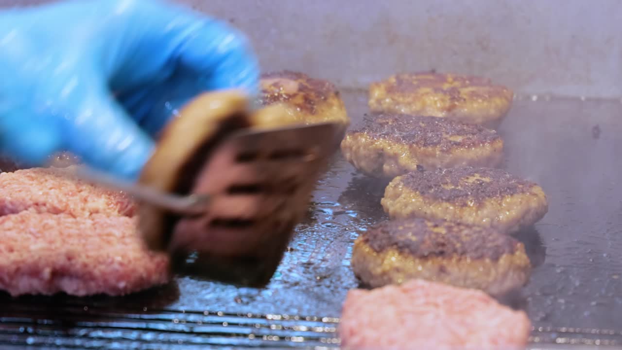 고기 패티는 뜨거운 프라이팬에서 요리됩니다. 스트리트 푸드, 셰프는 스파 ⁇ 라로 햄버거를 뒤집습니다.