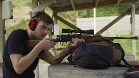 side portrait of a caucasian man wearing earmuffs, aiming at target using shotgun with optics mount at the shooting range