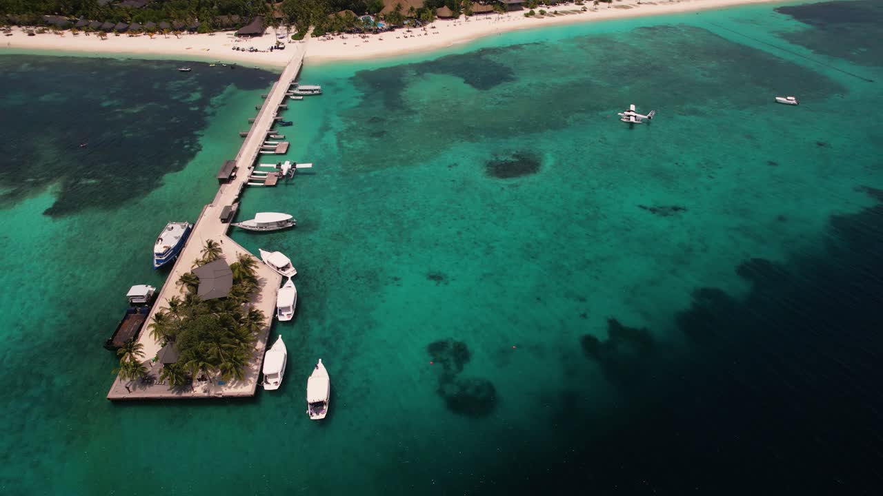 고요한 여름날 잔잔한 청록색 인도양에 있는 몰디브 쿠레두 섬의 부두에 천천히 접근하는 흰색 보트의 드론 샷