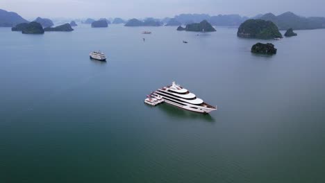aerial of large white mega yacht anchored in ha long bay vietnam surrounded by large limestone cliffs
