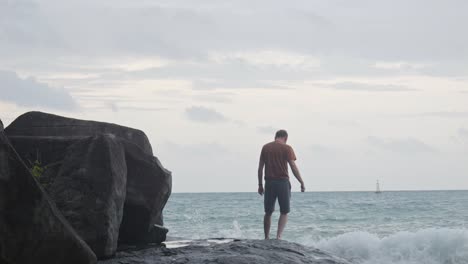 Blick-Hinter-Einen-Männlichen-Strandgänger,-Der-Vorsichtig-Auf-Nassem-Felsen-In-Richtung-Des-Welligen-Ozeans-Am-Strand-Von-Dam-Trau-In-Vietnam-Geht