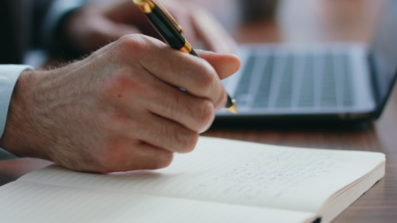 manos del jefe anotando información en el cuaderno trabajando en la computadora portátil de cerca. hombre escribiendo