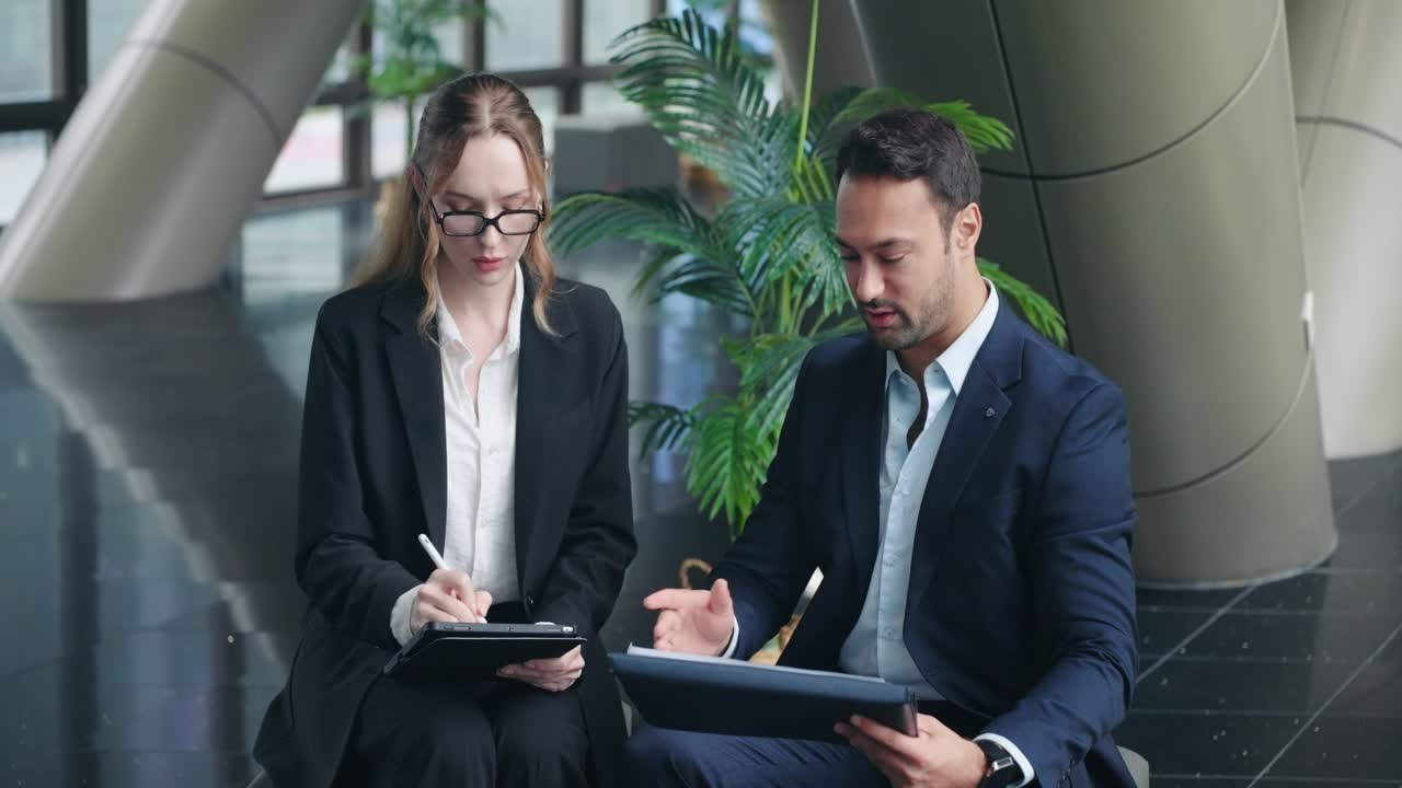Two Business Colleagues Sitting Close Together, Reviewing And Discussing Documents In Folders In The Workplace. - static shot