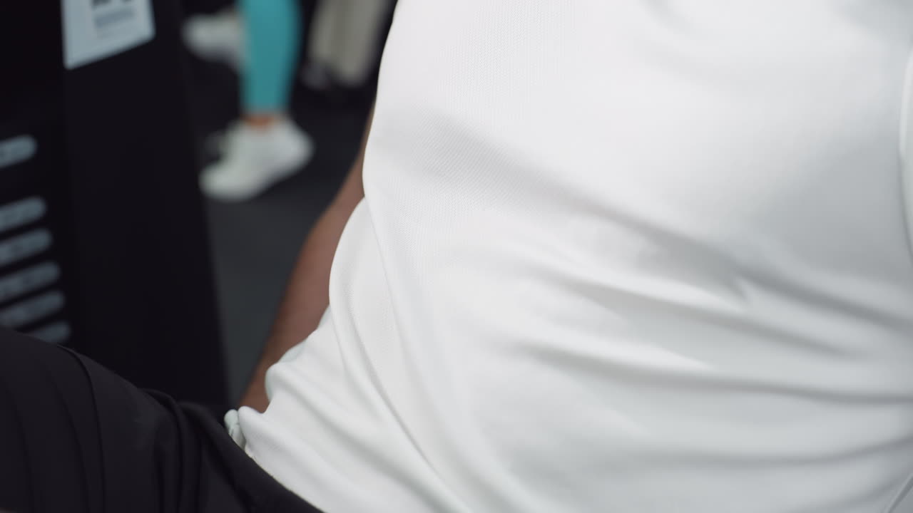 Close up of male trainer chest in white singlet straining under tension on leg press machine muscles flexing sweat glistening shirt pushing handles for powerful cardio strength training