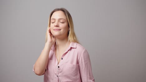 positive woman enjoys music with corded earphones on grey