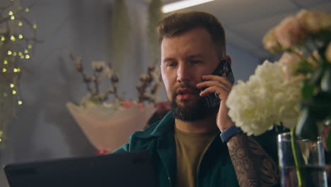 man taking a phone call while working with flowers and a laptop