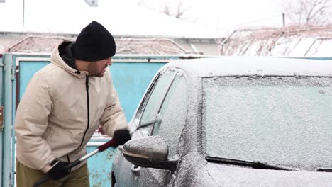 man scraping frost off the car window during winter