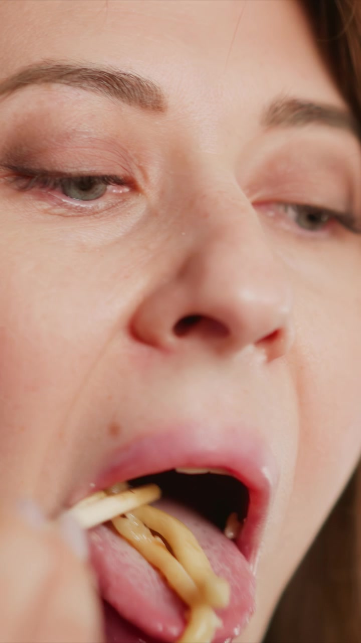 Primer plano de una mujer comiendo varios alimentos, centrándose en su boca y expresiones faciales. La secuencia muestra detalles de textura como labios, dientes con partículas de comida visibles durante el consumo y poros de la piel.
