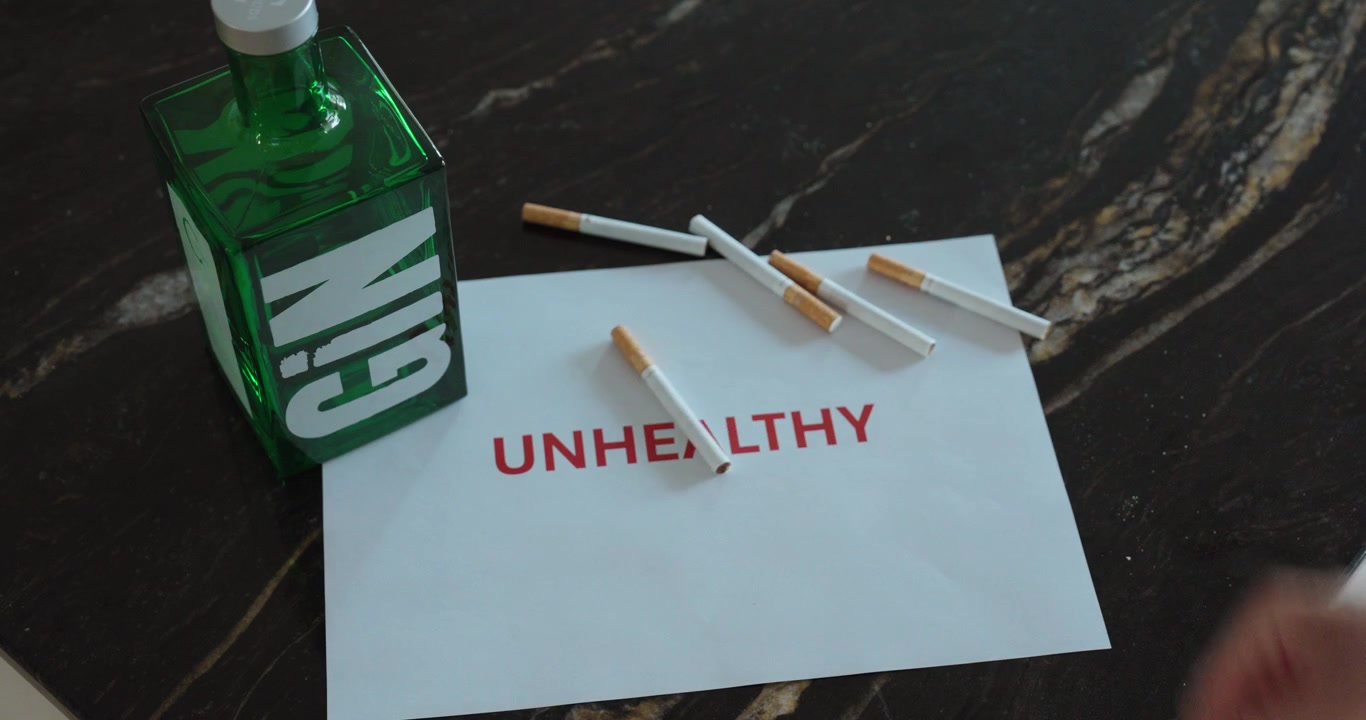 Close-up of a person throwing away cigarettes beside an alcohol bottle with an unhealthy warning message, representing addiction, lifestyle choices and health awareness.