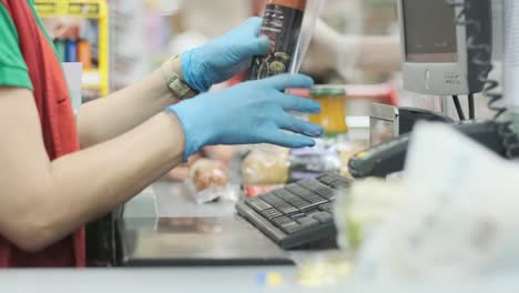 trabajador en la caja en el supermercado revisa los productos en guantes de goma en una cinta de productos básicos. protección contra la infección por coronavirus. preparación para la cuarentena.