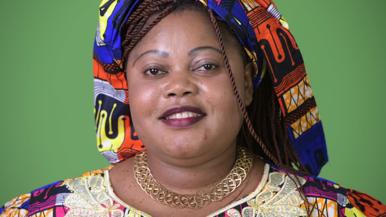 Overweight beautiful African woman wearing traditional clothing against green background