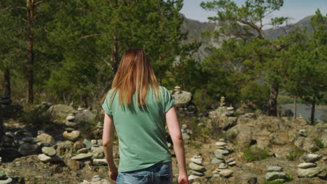 woman walks to stacked stones near pine forest at altai