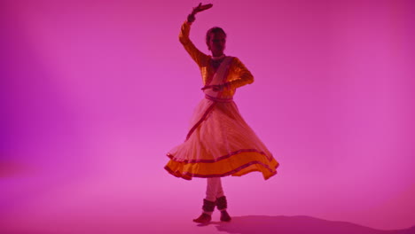 toma de estudio de larga duración de una bailarina de kathak que realiza un baile vestida con el vestido tradicional indio contra un fondo púrpura 3