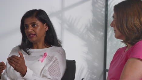 women wearing pink breast cancer awareness ribbons meeting and talking at therapy support group for cancer treatment patients with counsellor