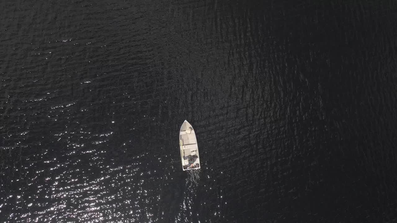 Aerial view of lone fisherman in hat and jeans on glistening black lake during springtime.