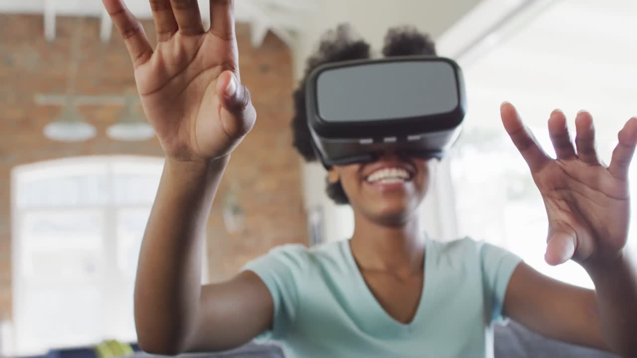 Happy african american teenage girl sitting on sofa, wearing vr headset and touching virtual screen