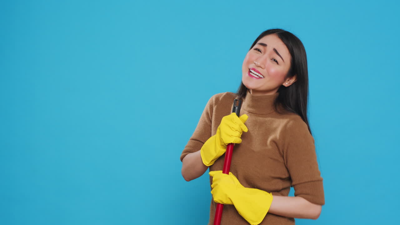 Happy housekepper dancing and having fun in studio while doing housecleaning using broom