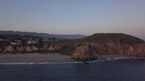 AERIAL:-flight-over-Malibu,-California-view-of-beach-Shore-Line-Pacific-ocean-at-sunset-with-mountain-cliff