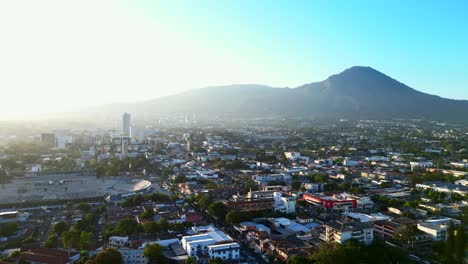 Aerial-view-large-sprawling-urban-city-with-mountain-backdrop-in-sun