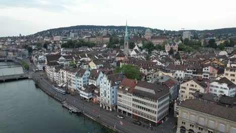 La-Iglesia-Del-Predicador-De-Zurich-Y-La-Orilla-Del-Río-Limmat-Con-El-Tren-Ligero-Pasando,-Suiza