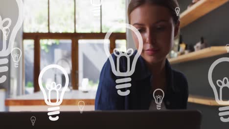 Animation-of-lightbulb-icons-over-caucasian-businesswoman-using-laptop