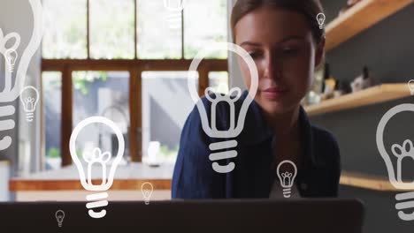 animación de iconos de bombillas sobre mujer de negocios caucásica usando portátil