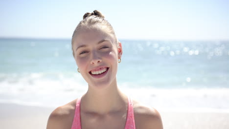 Eine-Junge-Kaukasische-Frau-Mit-Blonden-Haaren,-Trägt-Ein-Lässiges-Rosa-Oberteil-Und-Lächelt-Strahlend-Am-Strand