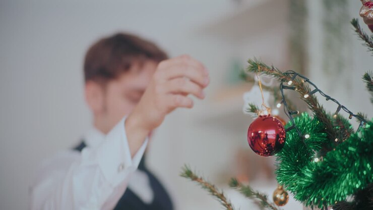 Handsome man hanging red bauble on illuminated Christmas tree