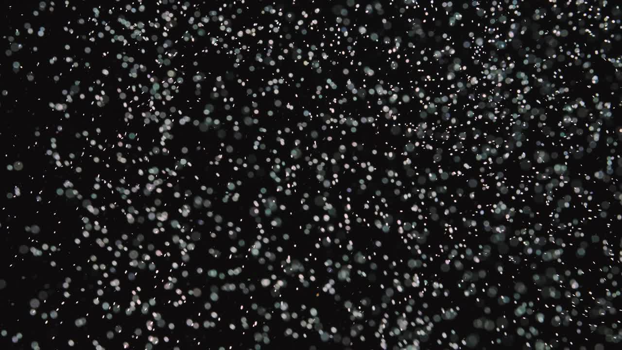 Particles in motion in the form of fine dust, round, white on a black background. Bokeh effect. Close up. Slow motion