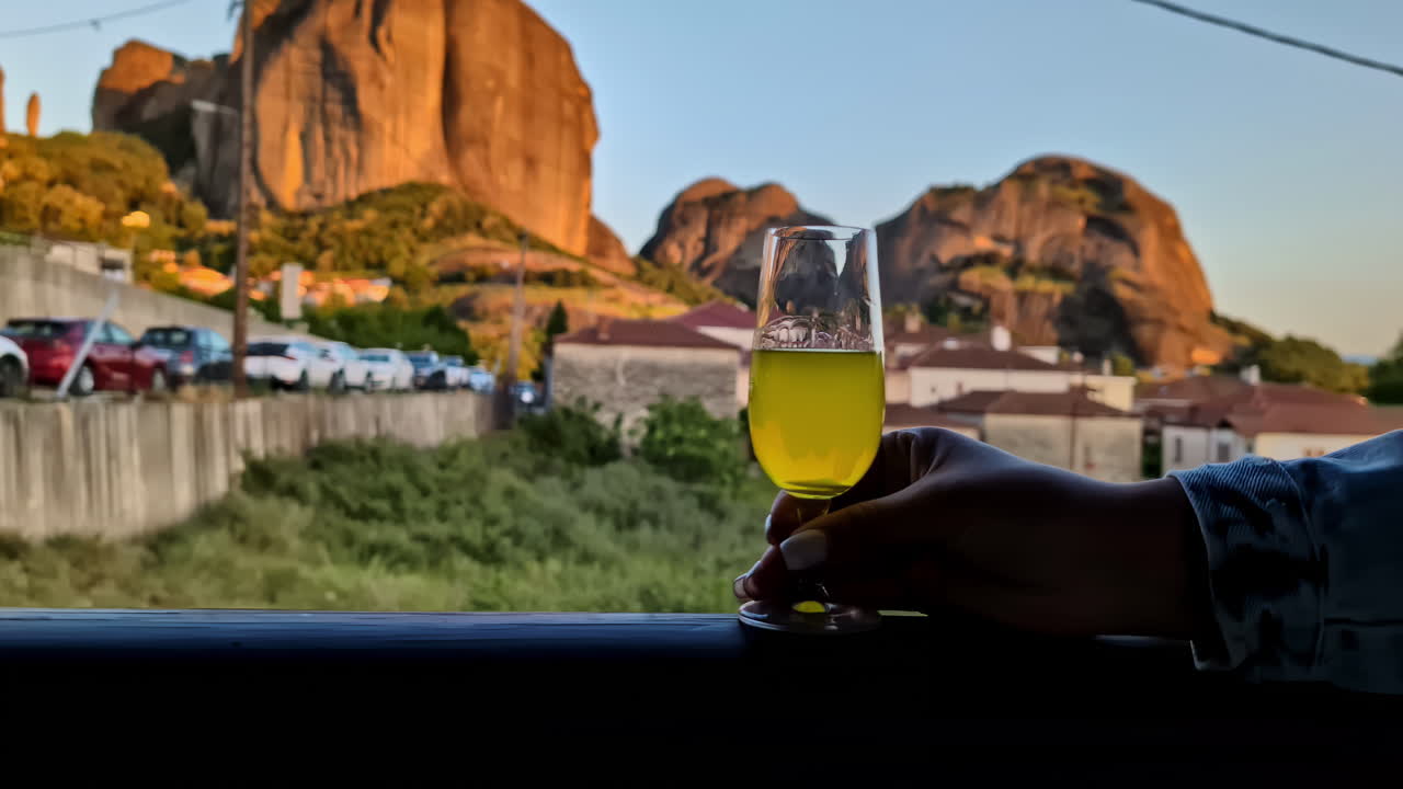 Hand holds amber drink in glass with warm glow on red rocks during golden hour near sunset