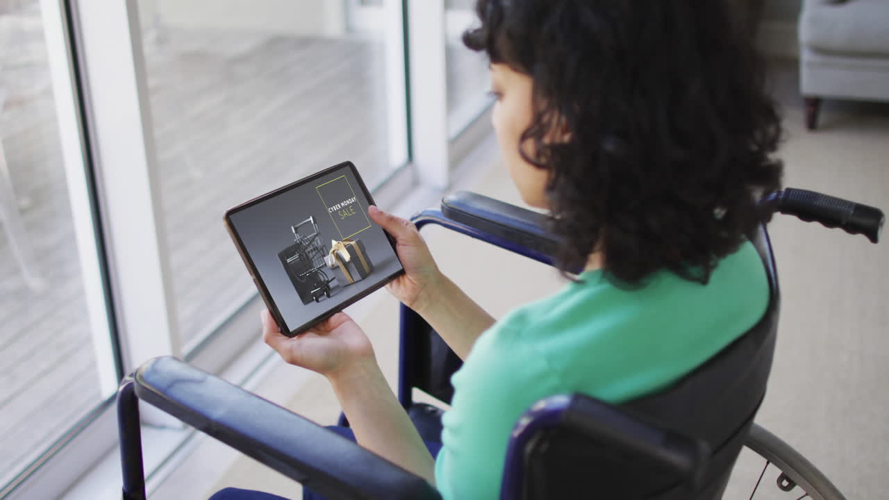 mujer biracial en silla de ruedas usando tableta, compras en línea en el lunes cibernético, cámara lenta