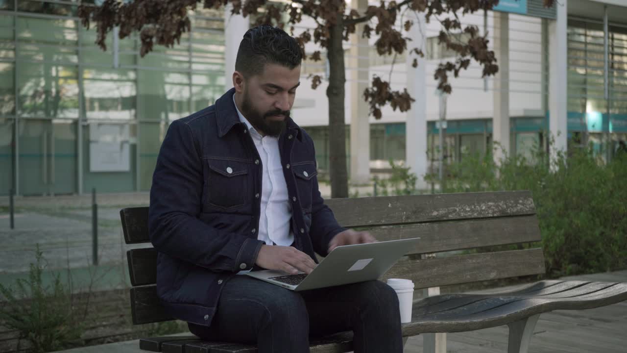 Man drinking from paper cup and using laptop on street