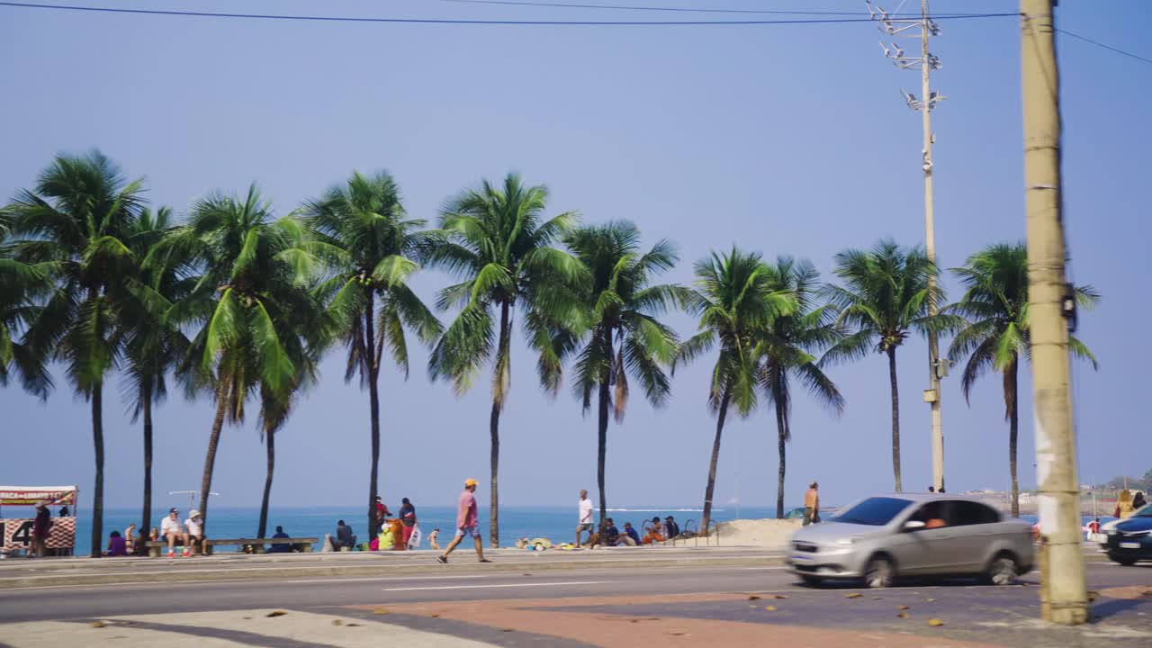 Giornata di sole con palme, turisti, auto sulla spiaggia di Ipanema a Rio de Janeiro, Brasile.