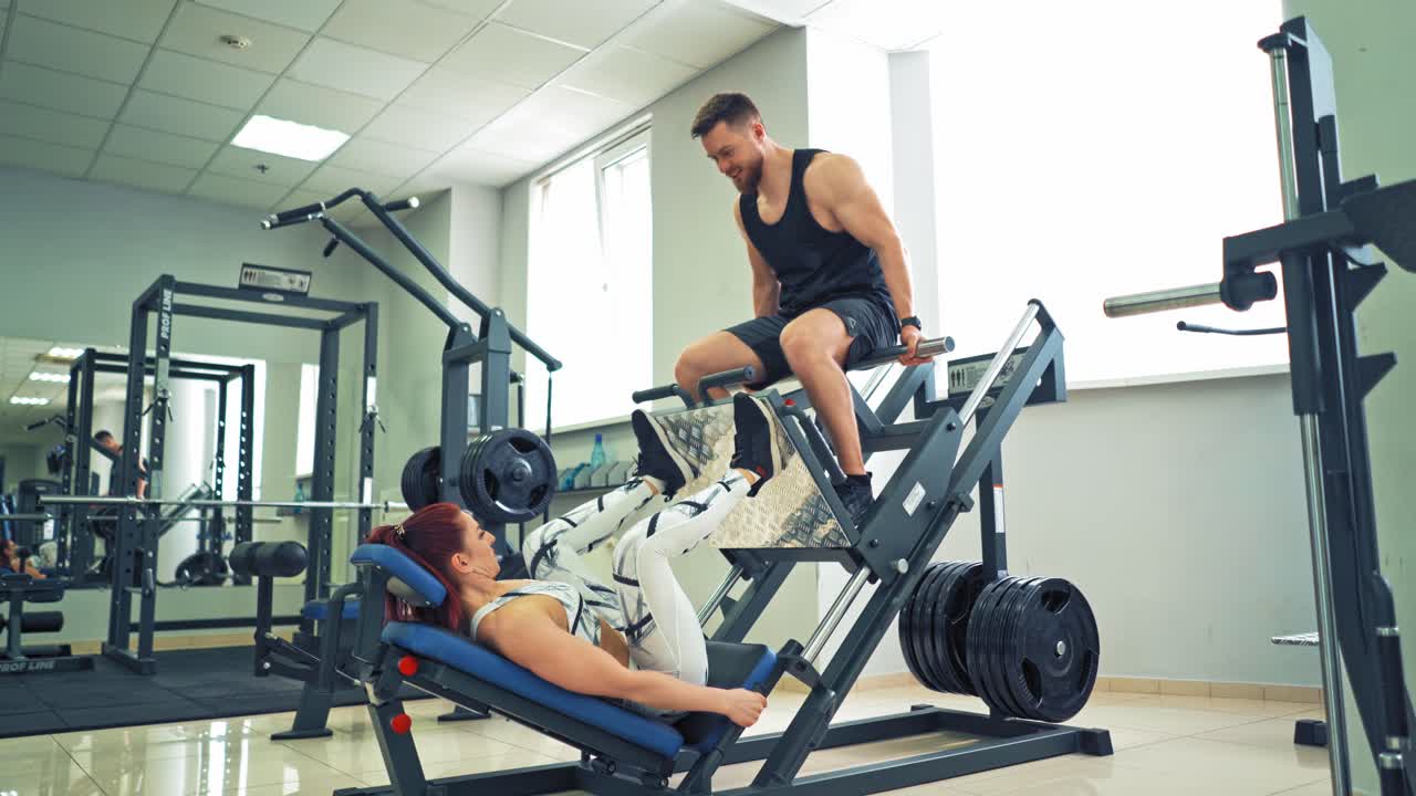 Woman weightlifter doing leg presses. Woman weightlifter doing leg presses with his trainer up on simulator