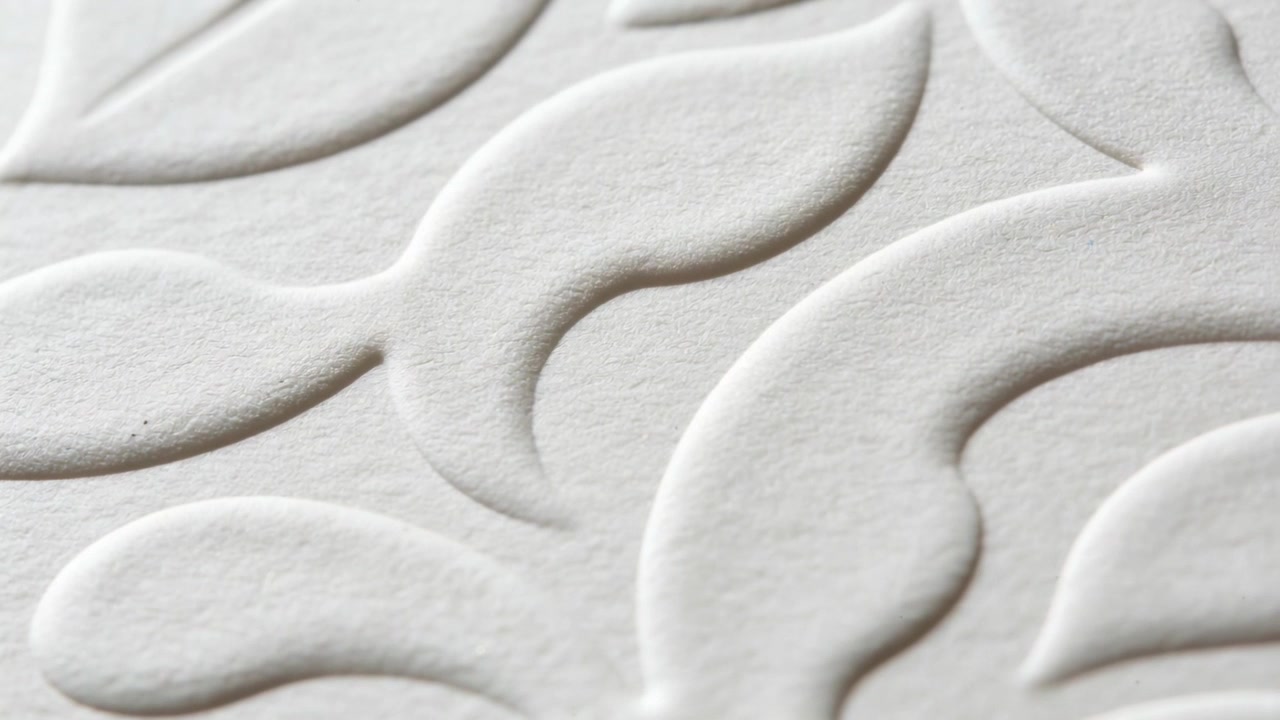 Tracking camera sliding down over embossed white paper on tabletop revealing leaf relief