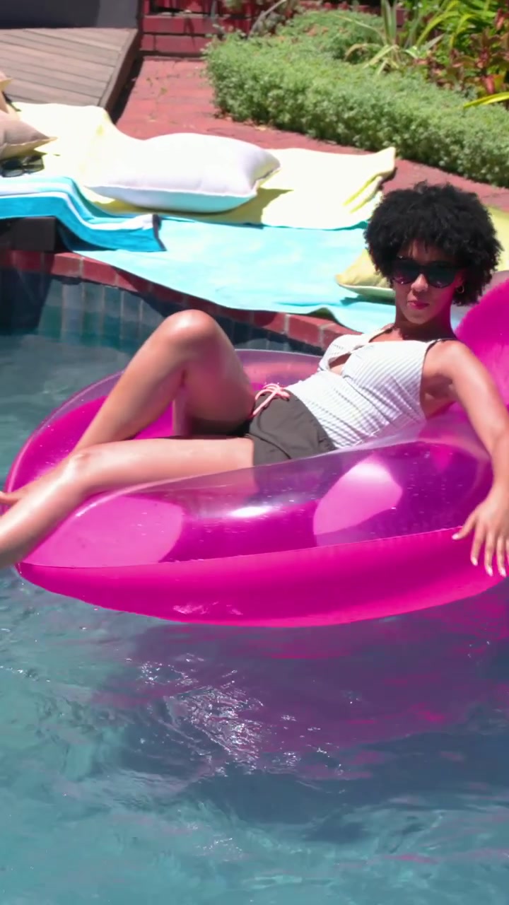 Reclining woman wearing shades and shorts moving on pink ring at home pool, touching man's hand