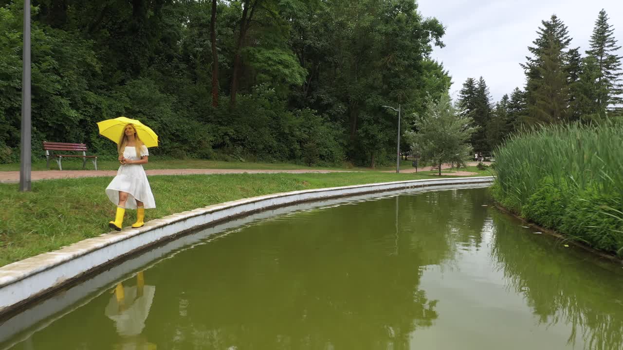 mujer con vestido blanco, paraguas amarillo camina cerca del lago con reflejo