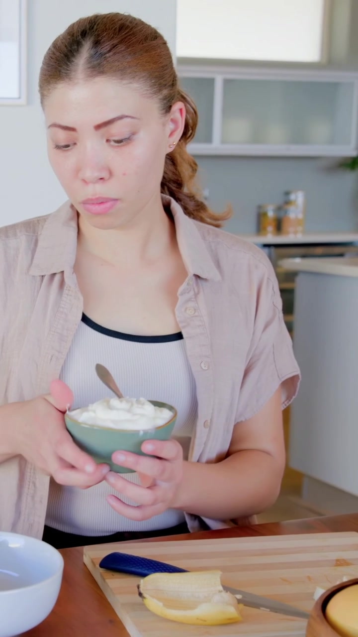 Vertical video: Stirring cook in tan top making yogurt at home, with green bowl banana, copy space