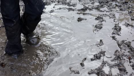 young child splashing in a muddy puddle, wearing waterproof clothing