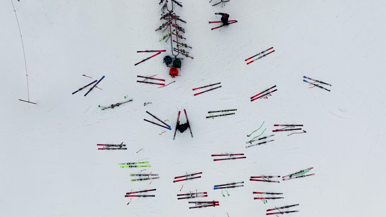 Aerial view of colorful skis scattered across the snow near a ski rack at the base of a mountain.