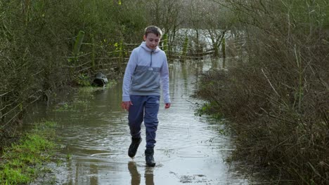 Young-farmers-boy-walking-along-a-flooded-country-path-and-wading-through-the-flood-lands