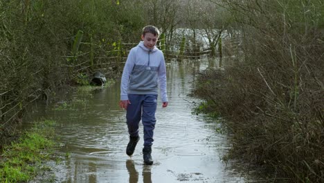 un joven granjero caminando por un camino inundado y atravesando las tierras inundadas.