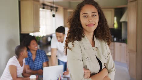 feliz mujer biracial en la cocina y mirando a la cámara con diversos amigos en el fondo