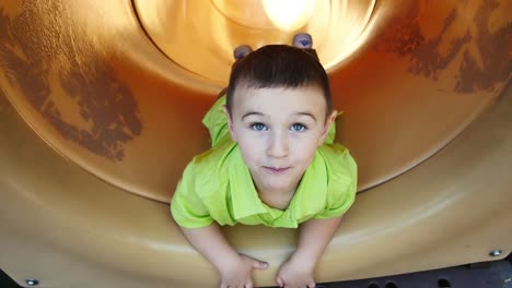 little boy pretends to fall off cliff inside yellow tube slide