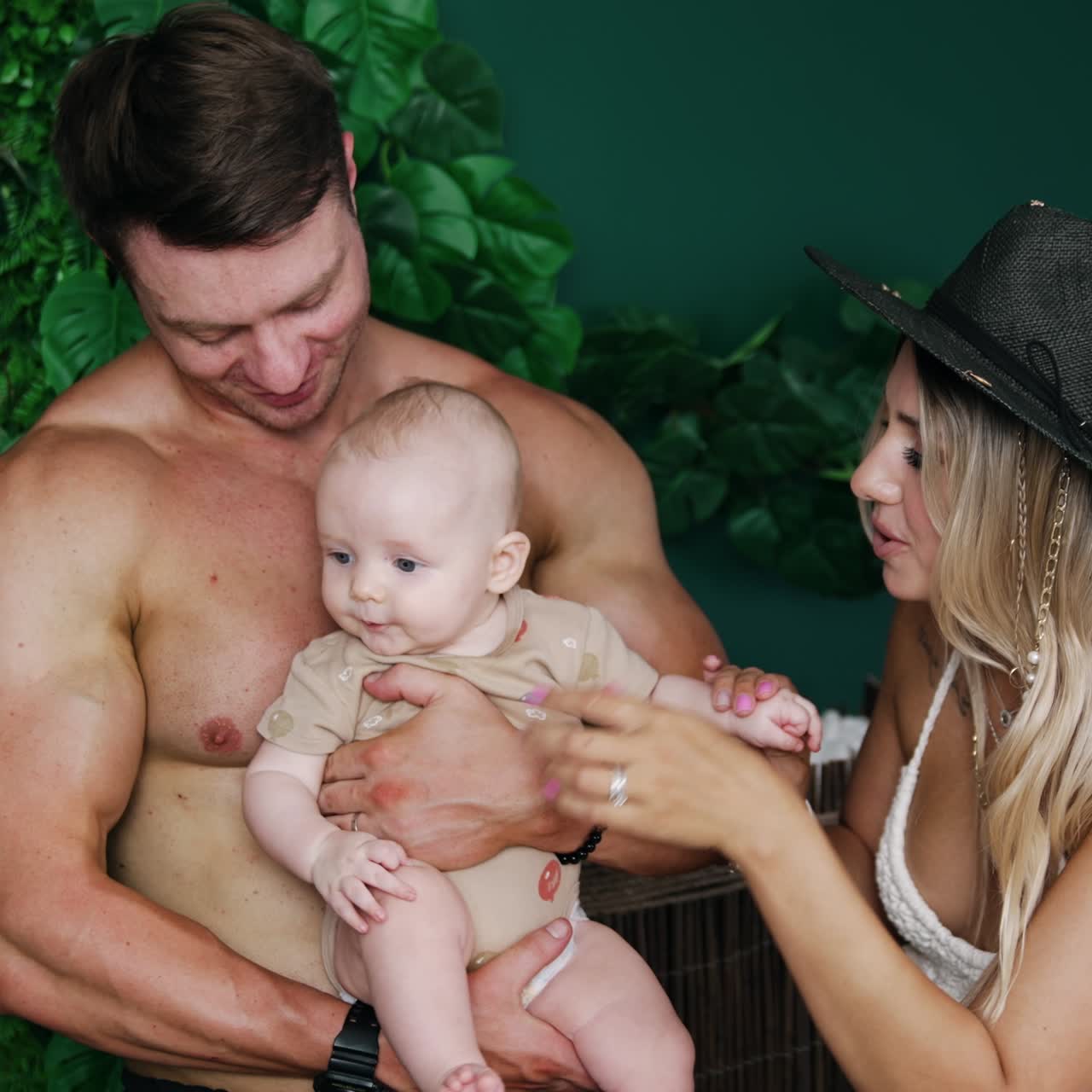Young Caucasian parents are on vacation with their infant. Father holds his tiny son and mom holds kid's hands