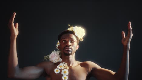 shirtless man adorned with flowers holding arms raised and looking up