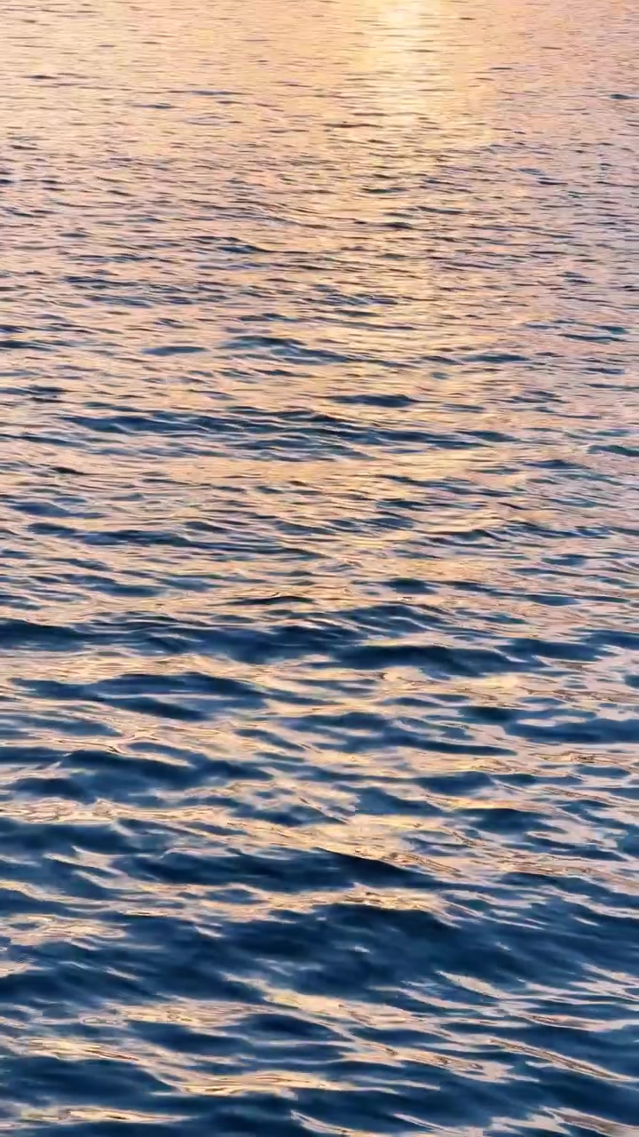 Waves on water reflect light at sunset. The sun sets over a body of water, creating ripples and reflecting warm light on the surface.