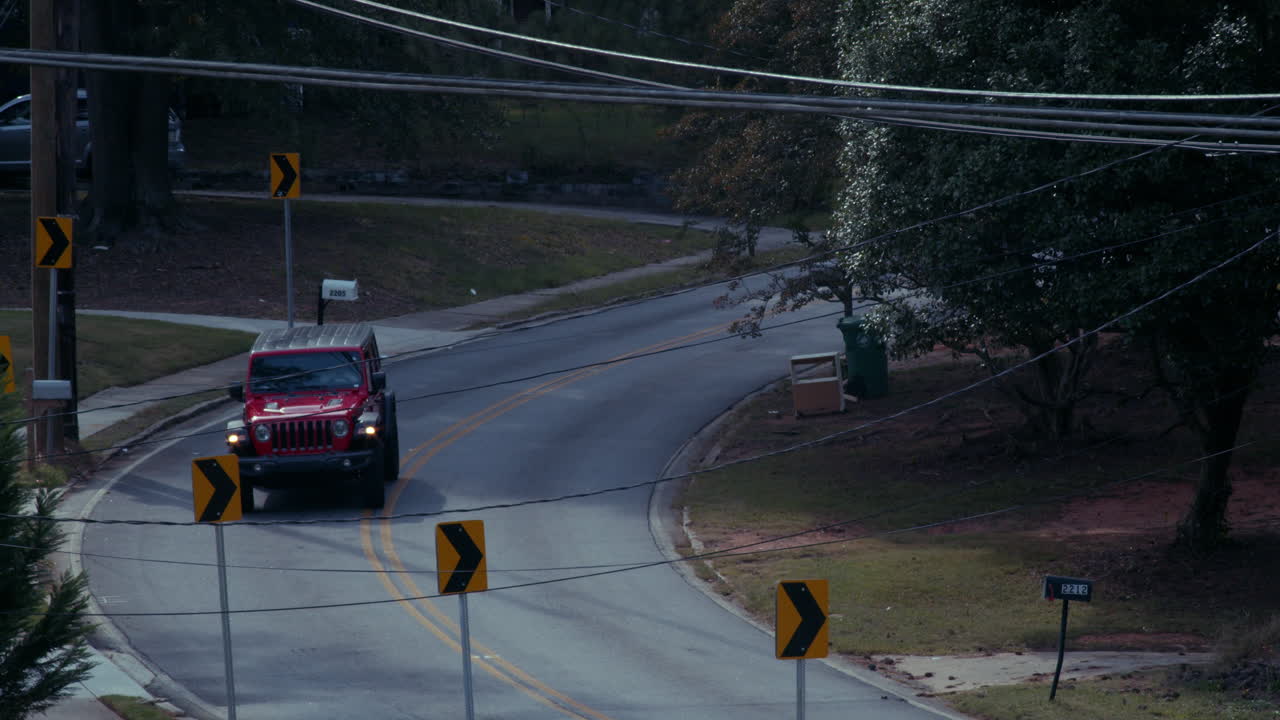 A red Jeep driving on a curved residential street with power lines